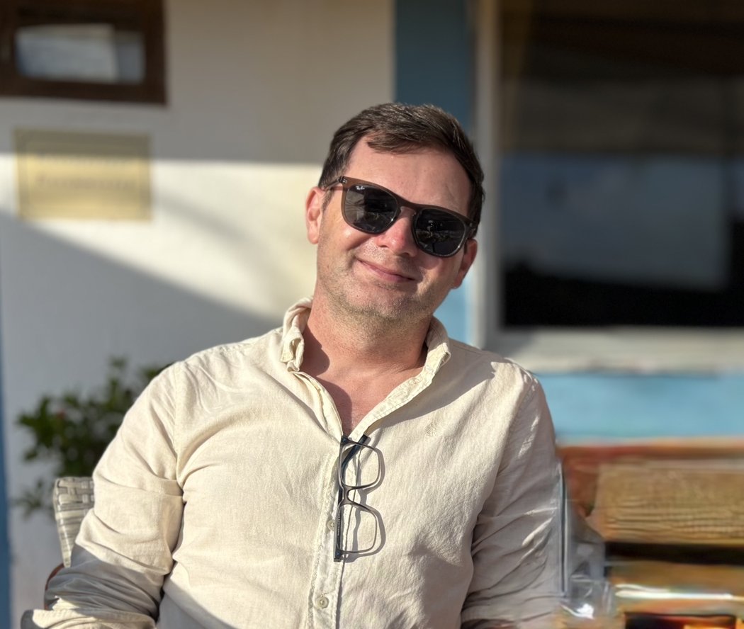 Russell sitting in sunlight, wearing sunglasses and a cream shirt